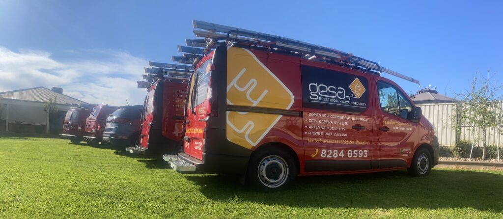 Red GESA Electrical & CCTV Solutions vans parked on green grass in Adelaide’s northern suburbs, showcasing professional service vehicles ready for electrical, CCTV, and data work.